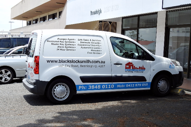 White van with blacks locksmith business branding and contact information parked in front of a building.