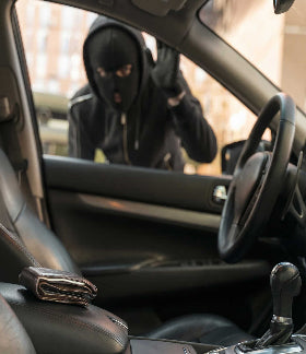 a thief wearing a black ski mask looking in to a car with a wallet on the seat
